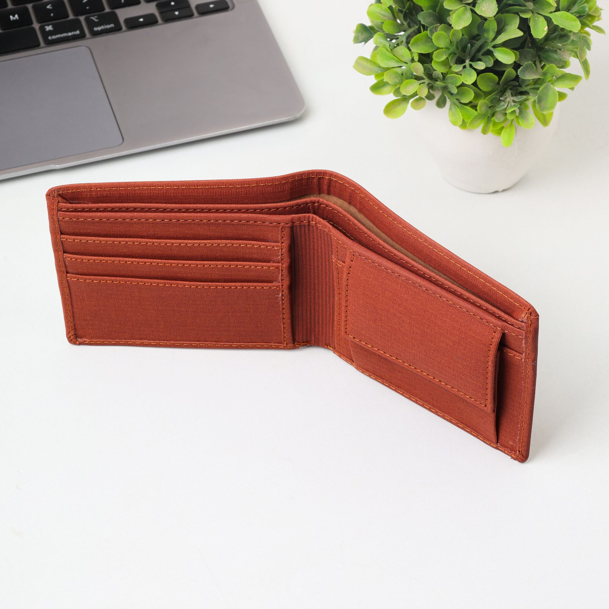 Open brown wallet placed on a white desk with a laptop and small plant in view, creating a minimalist office setup.